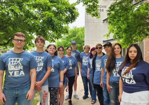 11 high school students stand outside of the Pappajohn Center building on a summer day