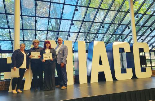 Two high school students hold a large certificate while standing next to a woman and a man in business attire